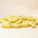 Close-up of scattered yellow vitamin tablets on a light neutral background.
